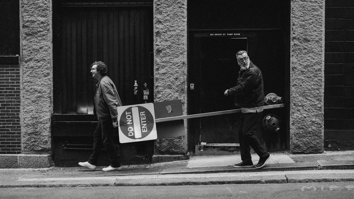 two men walk down the sidewalk carrying a "Do Not Enter" street sign